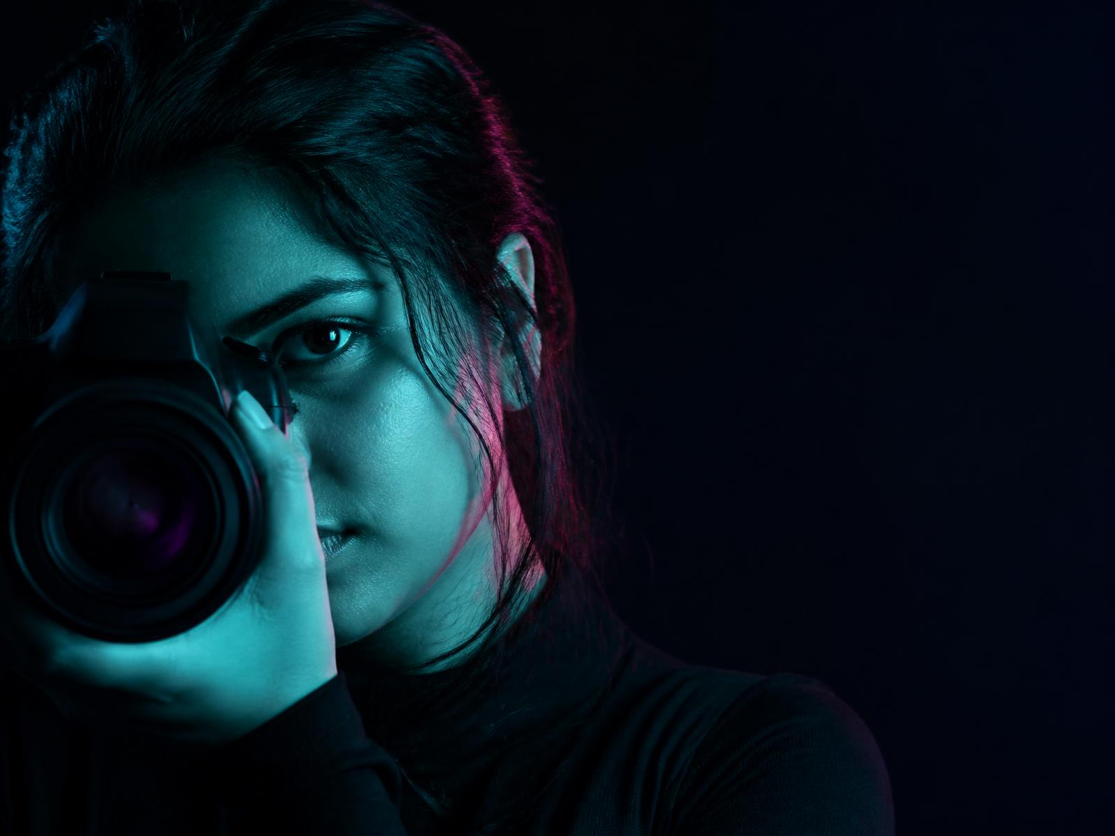 A photographer looking through a camera in cyan and magenta light